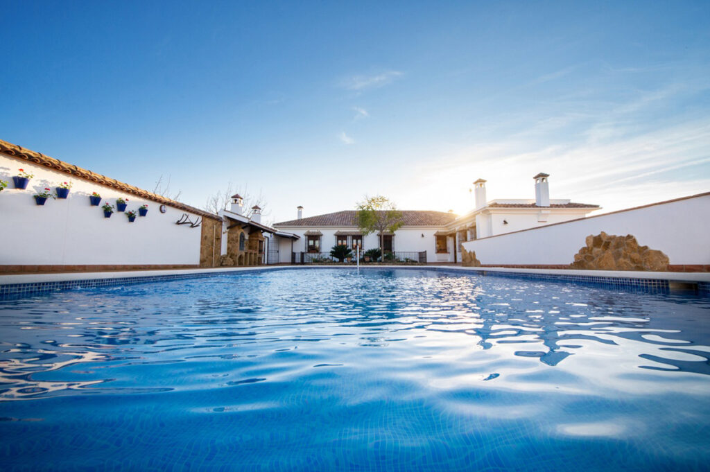 Primer plano de una piscina con una casa rural al fondo, muros blancos con flores